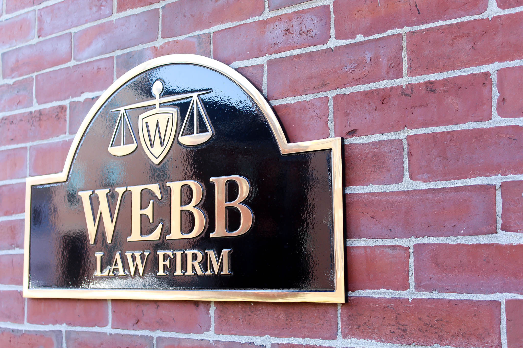 Webb Law Firm brass plaque mounted on red brick wall featuring scales of justice logo.
